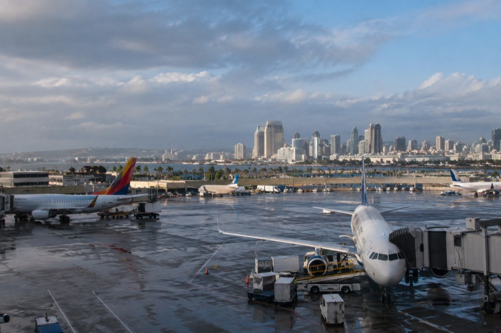 Airplanes parked at terminal gates at San Diego International Airport with downtown buildings in the distance
