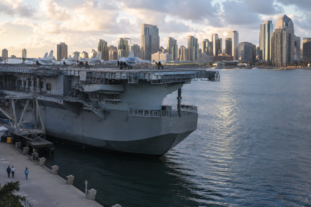 Aircraft carrier flight deck with downtown skyline across the bay in late afternoon light