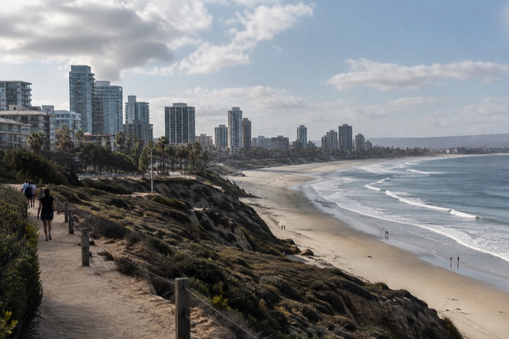 Coastal bluff trail above a wide sandy beach with waves in the distance