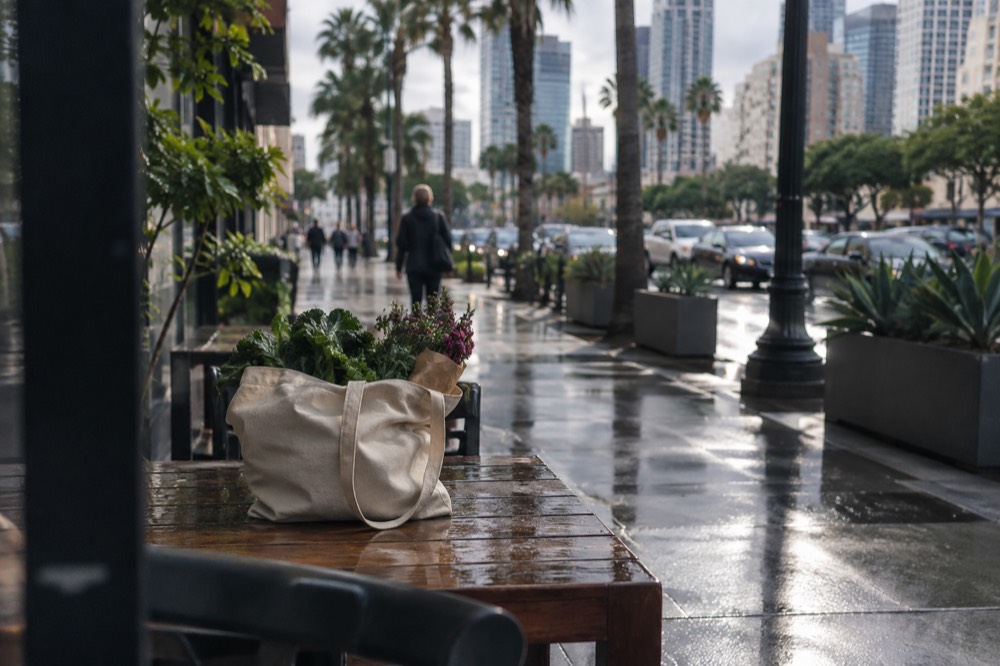 A canvas tote bag filled with greens and flowers on a wooden table