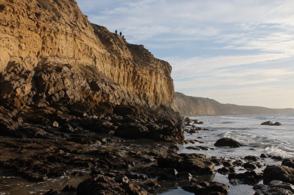 Golden cliffs above a rocky reef with tide pools at the base in late light
