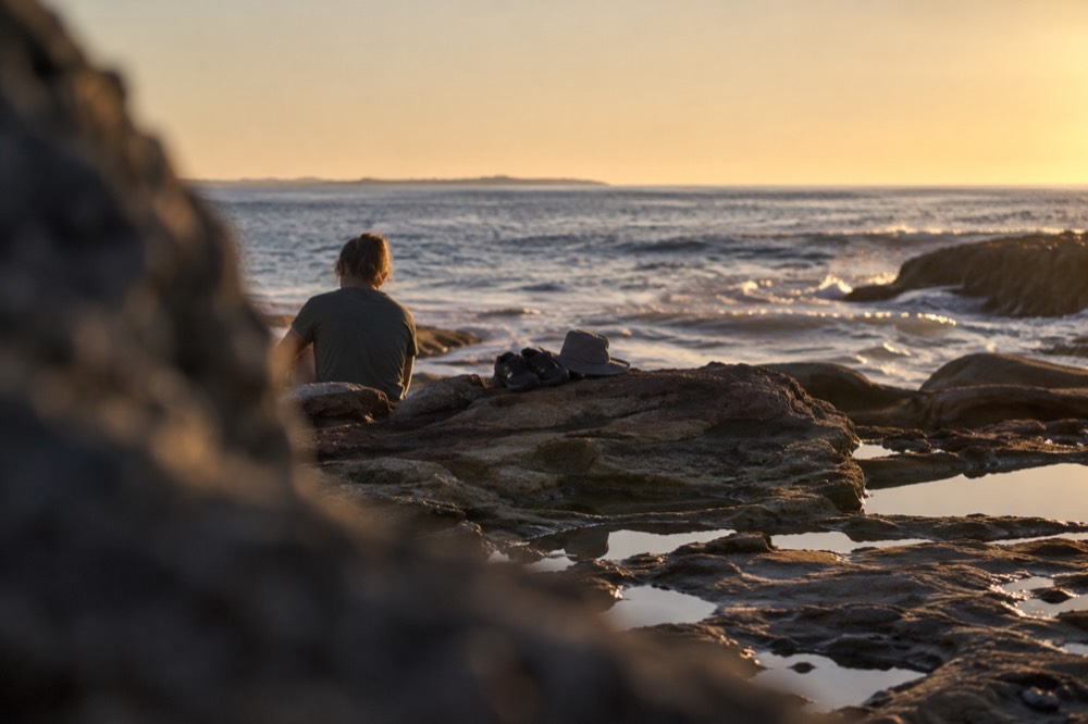 Closed-toe water shoes and a hat resting on a rock beside a tide pool