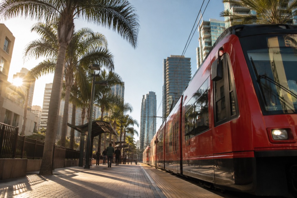 Red trolley vehicle at a downtown station platform with palm trees