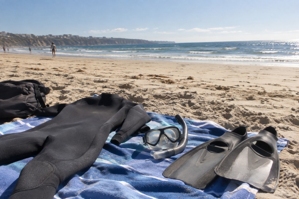 A wetsuit, mask and fins laid out on a beach towel near the sand