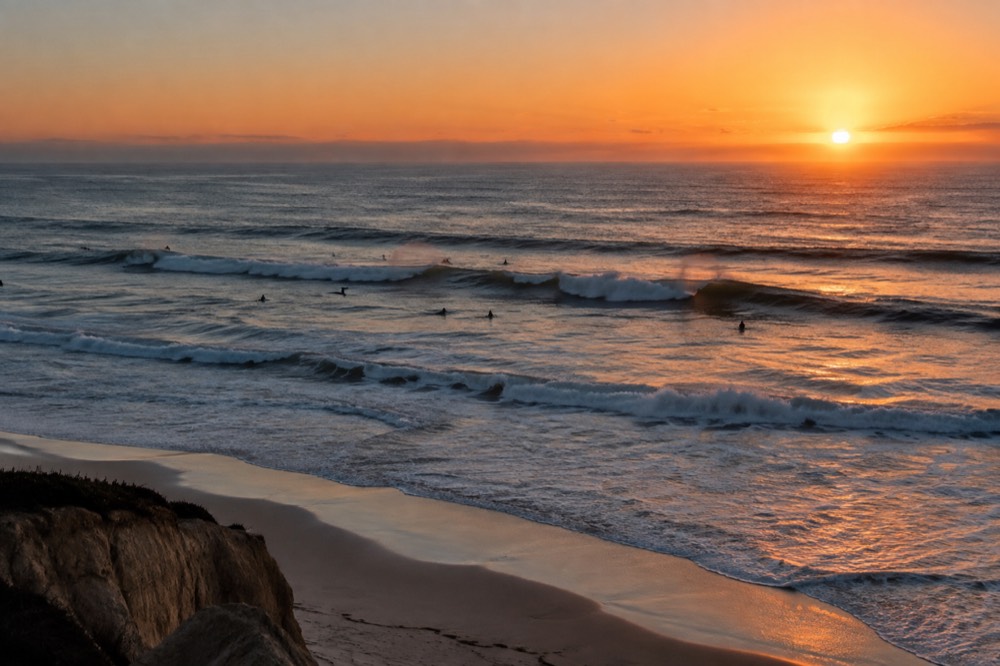 Large rolling waves at sunset with silhouetted surfers waiting beyond the break
