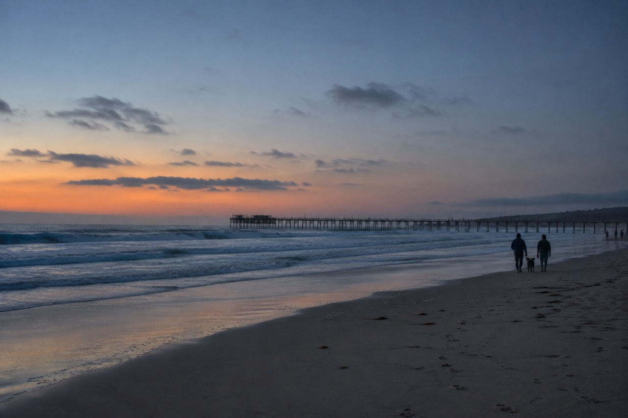 Waves rolling toward a wide sandy beach with a long pier in the distance