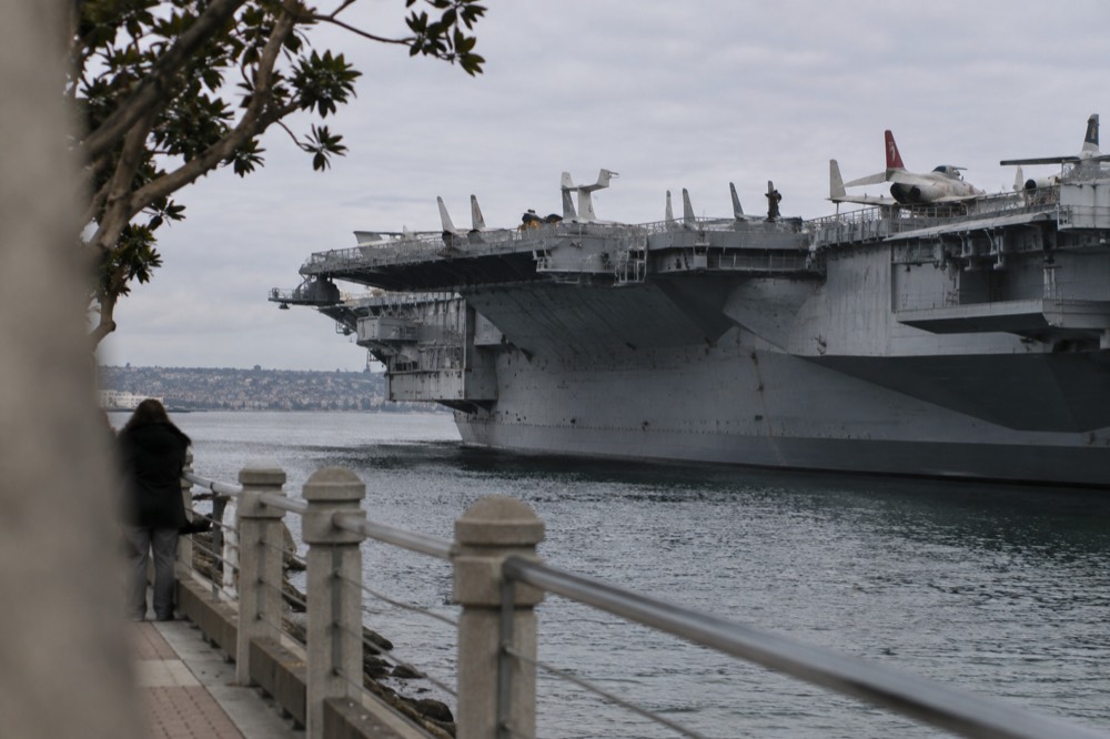 The flight deck of an aircraft carrier covered with vintage jets and a harbor view