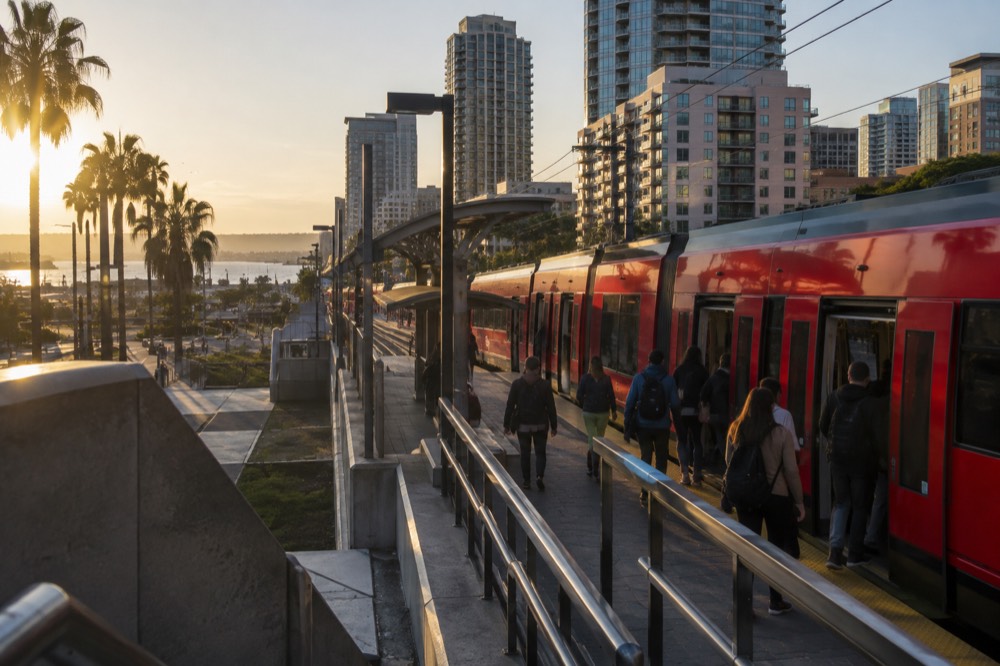 A red trolley car at a downtown San Diego station with passengers boarding