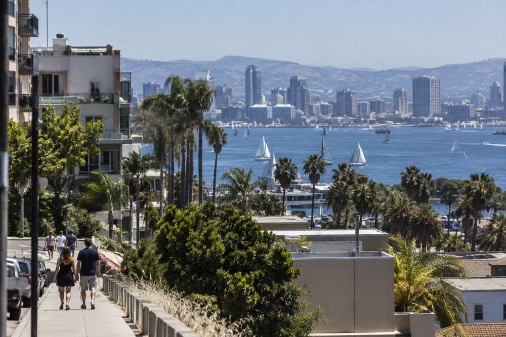 Sunlit San Diego bay with sailboats and a distant city skyline on a clear summer morning