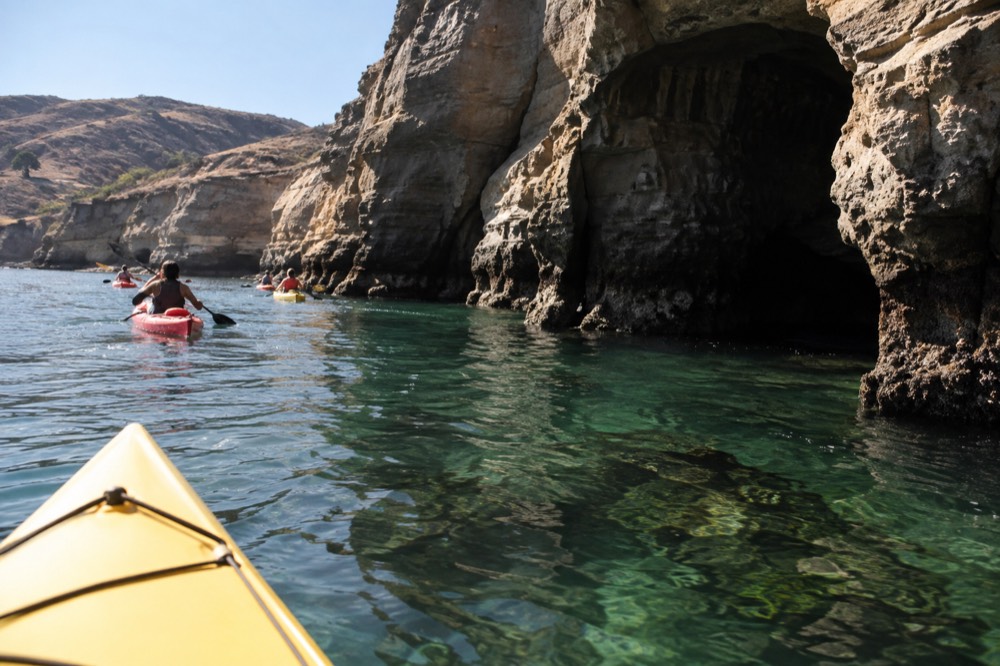 Kayaks floating beside sandstone sea caves at La Jolla with clear green water