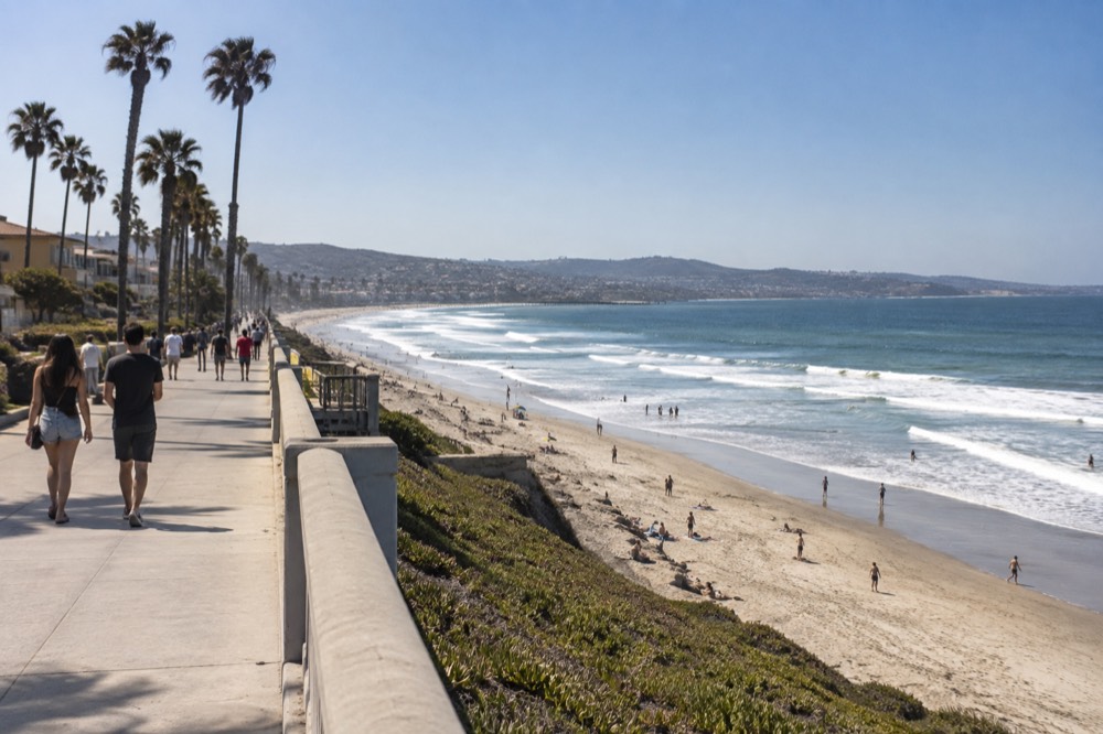 Pacific Beach boardwalk on a sunny July afternoon with palm trees and rolling surf