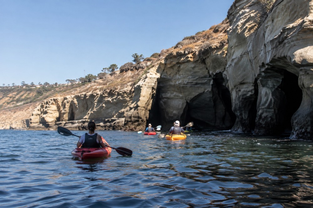 Kayakers paddling toward sandstone cliffs and sea caves along the La Jolla coastline