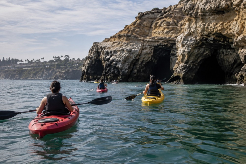 Kayaks paddling across calm green water toward La Jolla sea caves