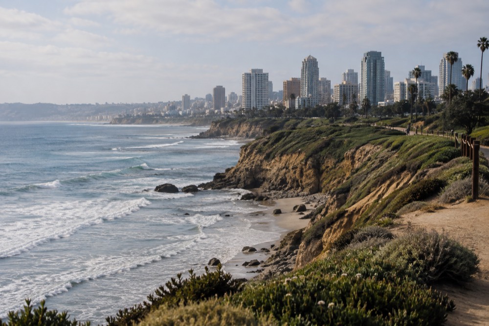Green cliffs above the San Diego coastline with waves rolling in under a soft morning sky
