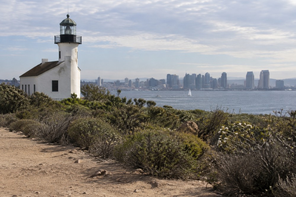 A historic lighthouse tower standing above green coastal scrub