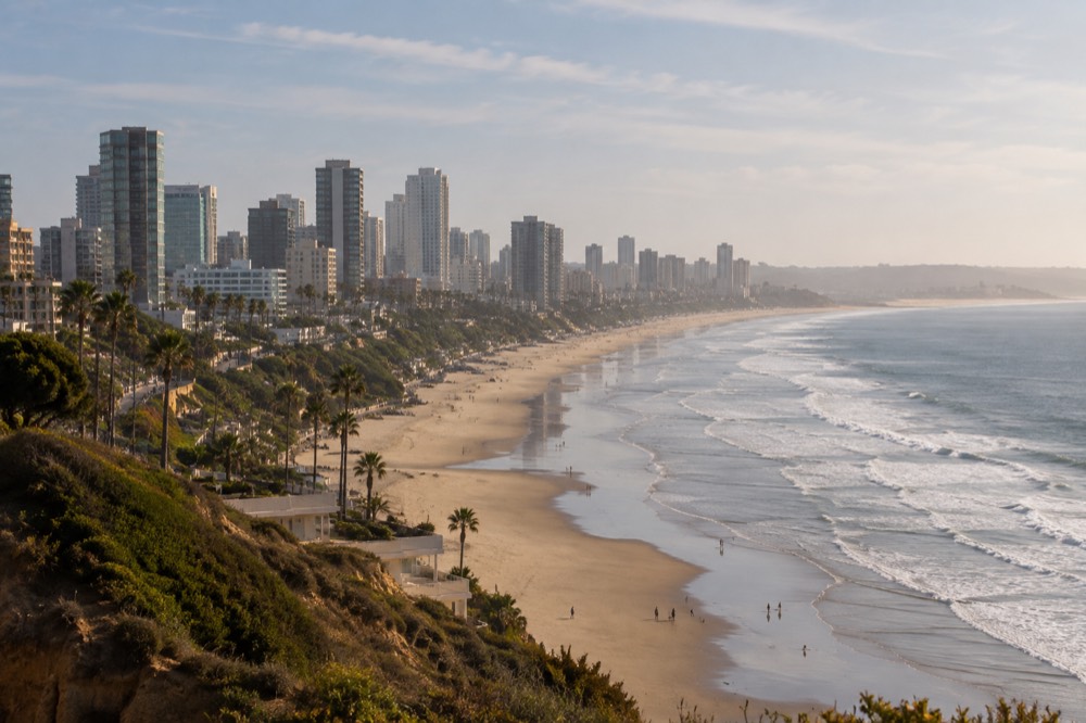 A wide sandy beach at low tide with gentle waves and soft morning light