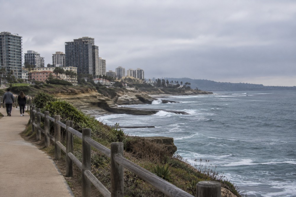 A coastal walking path above the ocean with waves breaking on rocky cliffs