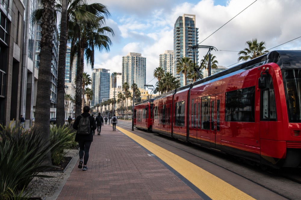 Red trolley parked at a downtown San Diego stop with the skyline behind it