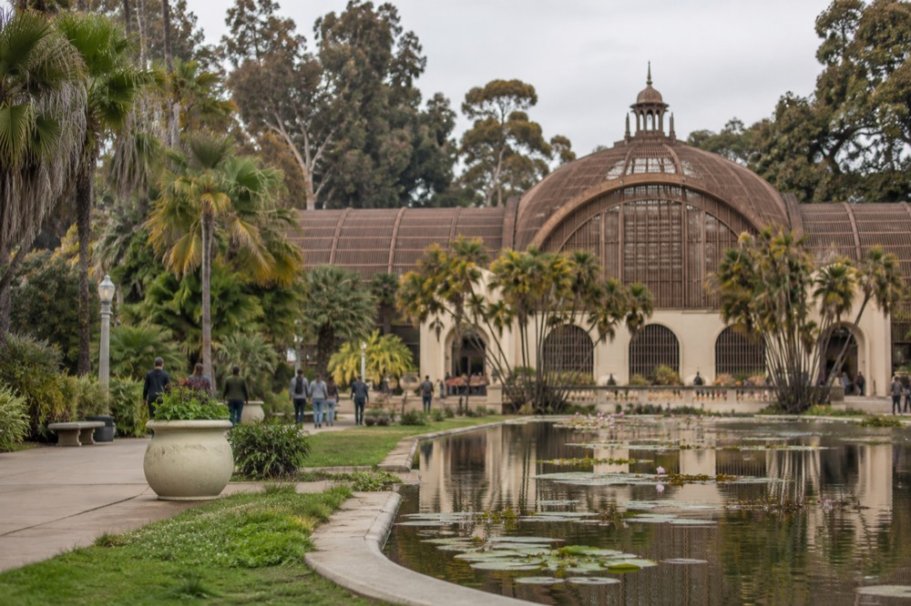 Wooden lath botanical building beside a lily pond in a public park with visitors strolling the path