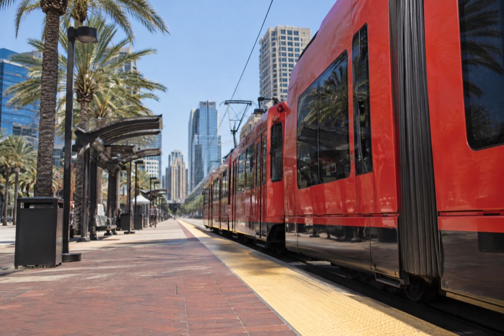 Red trolley at a downtown station with palm trees and office buildings behind