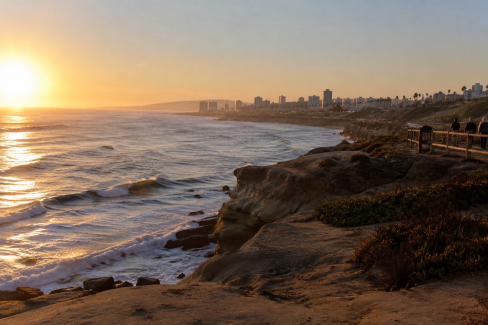 Ocean waves breaking against sandstone cliffs at a coastal sunset viewpoint