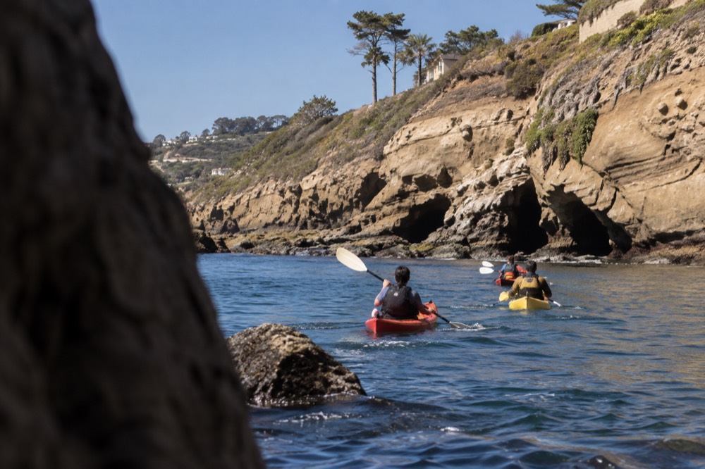 Kayaks along a rocky La Jolla shoreline with caves in the cliff