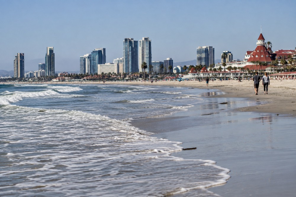 A wide sandy beach with gentle waves and a historic hotel in the distance